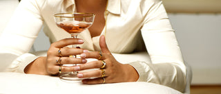 Eine Frau mit mehreren verschiedenen Ringen hält ein Glas mit alkoholischem Getränk.